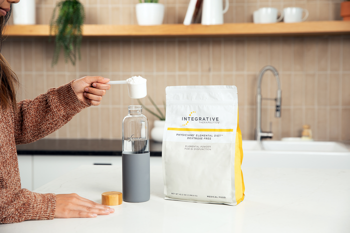 Person about to pour a scoop of Physicians' Elemental Diet into a bottle of water